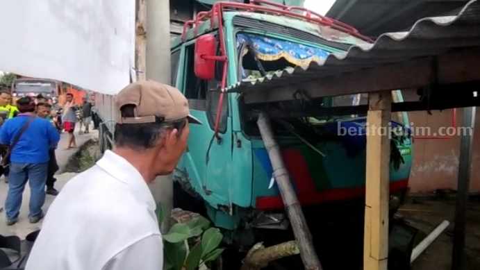 Kondisi truk box tronton nopol L 9194 AN yang menabrak dua teras rumah warga dan toko onderdil sepeda motor di Jalan Raya Trowulan, Kecamatan Trowulan, Kabupaten Mojokerto. [Foto : Misti/beritajatim.com]