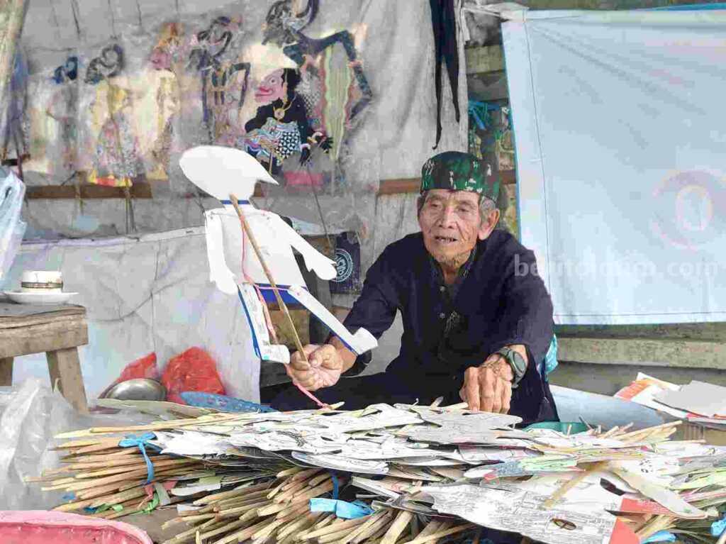 Mbah Jhony, Penjual Mainan Wayang Kertas yang Tak Tergilas Zaman Mbah Jhony, penjual wayang kertas sedang memperagakan pertunjukan wayang