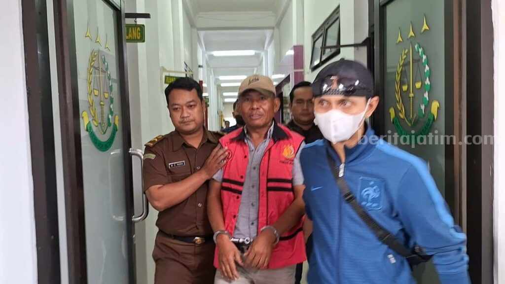 Tersangka yang merupakan Kades Lolawang di Kecamatan Ngoro, Kabupaten Mojokerto saat dibawa ke mobil tahanan Kejati Kabupaten Mojokerto. [Foto : Misti/beritajatim.com]