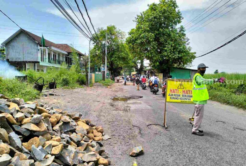 Warga sekitar membantu mengamankan arus lalu lintas saat perbaikan jalan berlangsung.