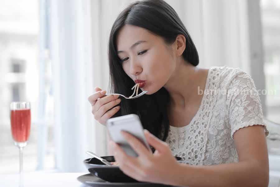 Ilustrasi perempuan sedang menggunakan ponsel sambil makan (foto: Andrea Piacquadio, pexels)