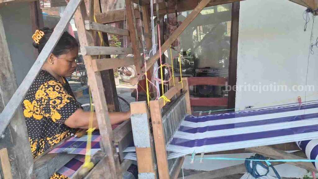 Perajin sarung tenun Kani (49) saat melakukan aktivitas pembuatan kain tenun di depan rumahnya di Dusun Cinandang, Desa Cinandang, Kecamatan Dawarblandong, Kabupaten Mojokerto. [Foto : Misti/beritajatim.com]
