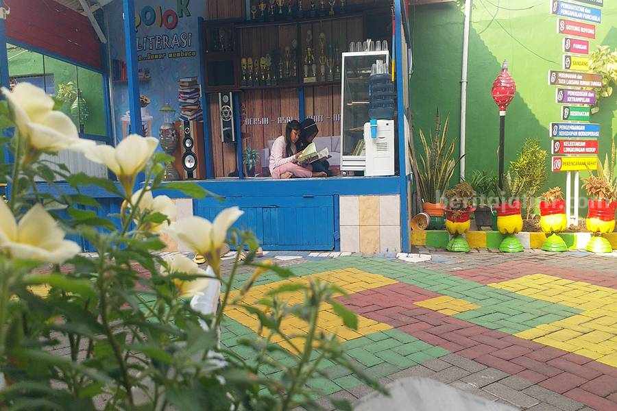 Dua anak sedang membaca koleksi buku di pos perumahan Bluru Permai Sidoarjo.