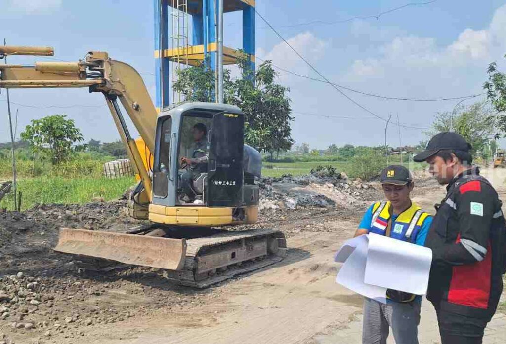 Perbaikan Jalan Banter-Kalipadang Gresik Dikebut Dua orang pekerja dan alat berat sedang melakukan perbaikan jalan yang rusak akibat diterjang banjir anak sungai kali Lamong