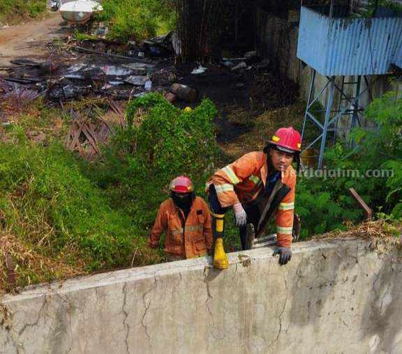 Petugas Damkarla Gresik memanjat pagar usai memadamkan api yang membakar lahan kosong di dekat pabrik