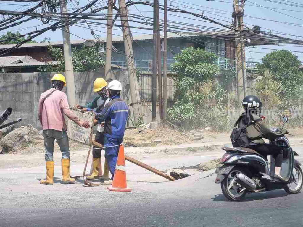 Tiga pekerja proyek sedang memasang garis pembatas pada jalan aspal yang menggelembung