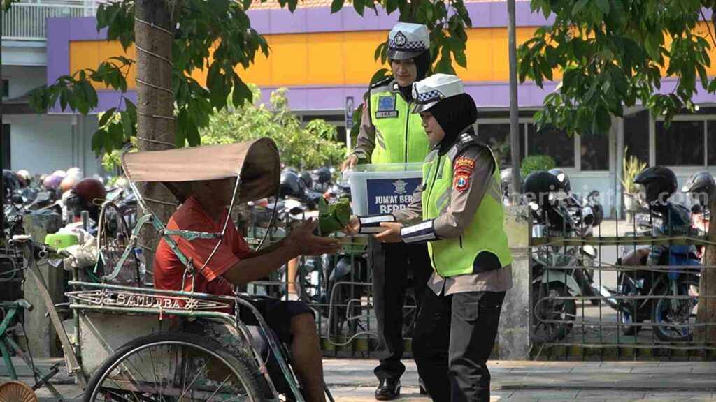 Dua orang polwan sedang membagikan nasi bungkus gratis kepada tukang becak yang sedang menunggu penumpang