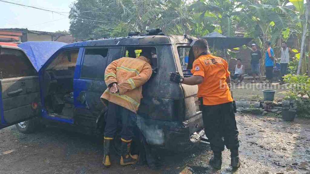 Caption : Kondisi mobil Mitsubishi Kuda nopol B 1613 JQ warna biru yang terbakar. [Foto : Misti/beritajatim.com]