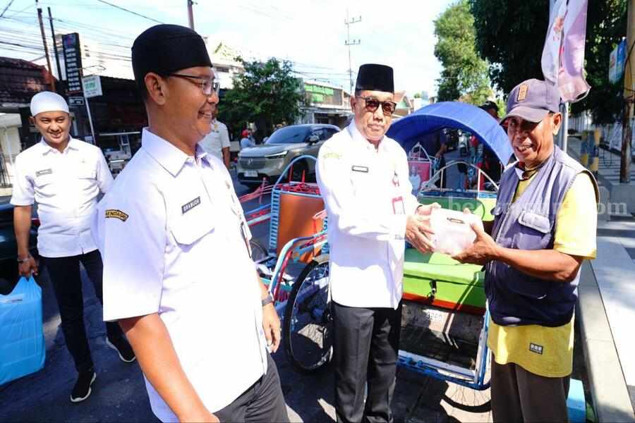 Sekda Banyuwangi Mujiono menyerahkan daging hewan kurban kepada tukang becak di depan Kantor Bupati