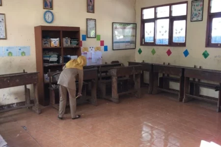 Seorang guru sedang membersihkan ruang kelas 1 di SDN Setono yang masih kosong pendaftar. (Foto/Istimewa)