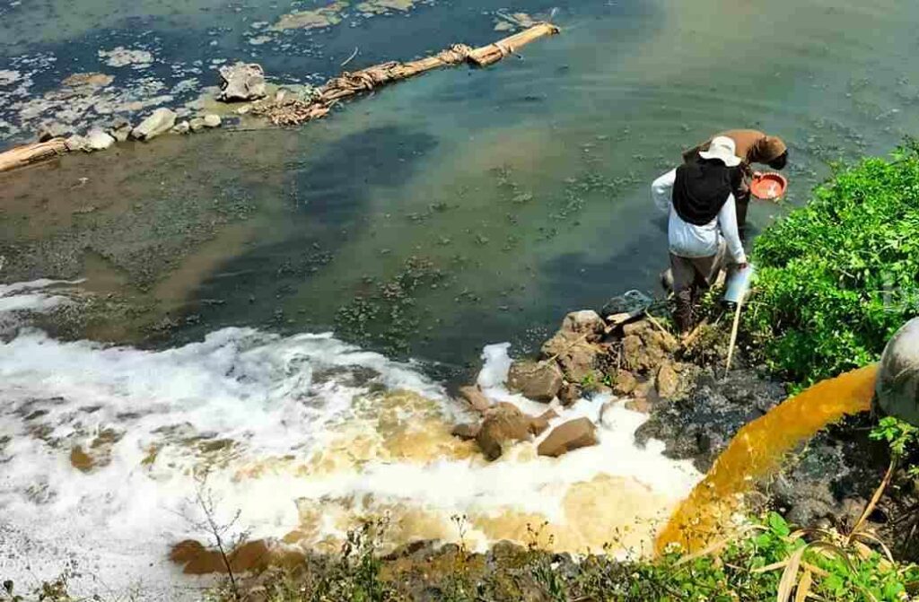 Foto dua orang sedang mengambil sampling air yang tercemar limbah.