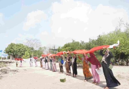 Foto para lansia membentangkan bendera di pinggir pantai.