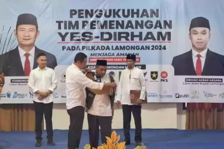 Yuhronur Efendi secara simbolis memasangkan jaket kepada Ketua Tim Pemenangan, Imam Mukhlisin, saat pengukuhan di aula Hotel Mahkota Lamongan, Sabtu (7/9/2024).