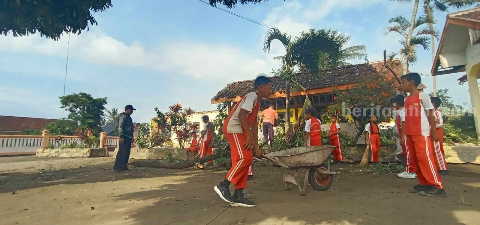 Murid SDN Sumberagung 2 membersihkan puing-puing bangunan yang terbang dibawa angin puting beliung, Jumat (1/11/2024). (Foto : Winanto/beritajatim.com)